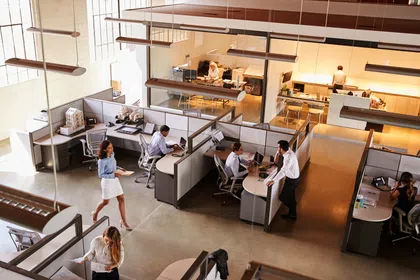 Modern office interior with employees working at desks and collaborating in a bright, open space.