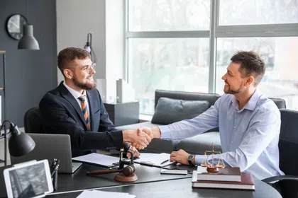 Two business professionals shaking hands in a modern office setting with legal elements present.