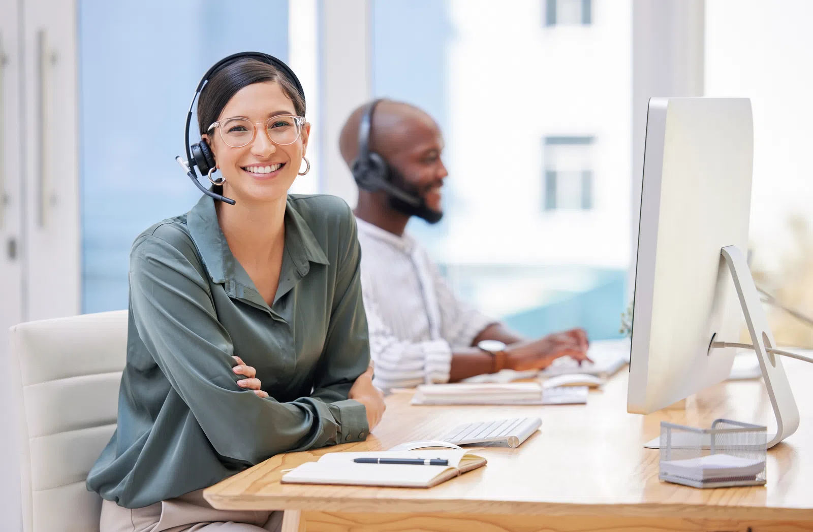 Two customer service agents at desks, smiling while using headsets in a modern office environment.