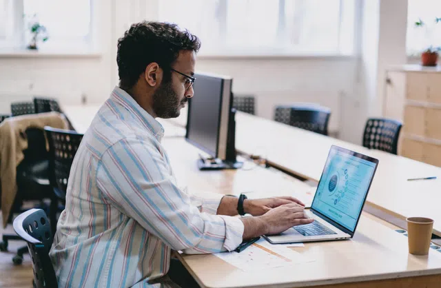 Professional man working on a laptop in a modern office environment with natural light.