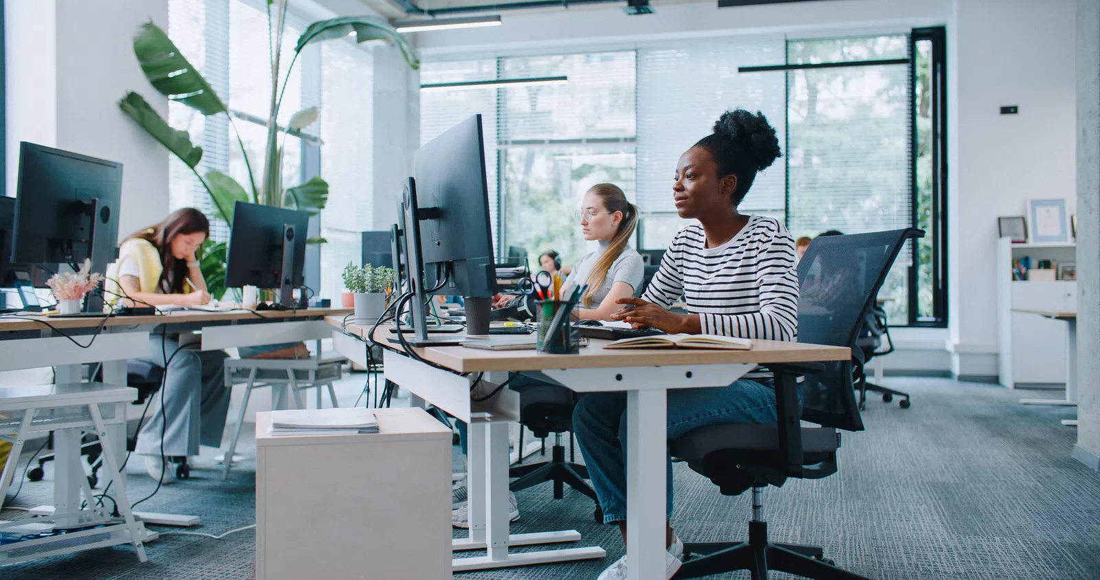 Women working collaboratively in a modern office space with computers and plants.