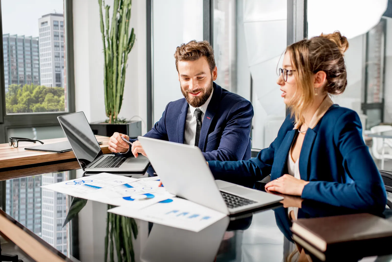 Business professionals collaborating in a modern office with laptops and documents on a glass table.