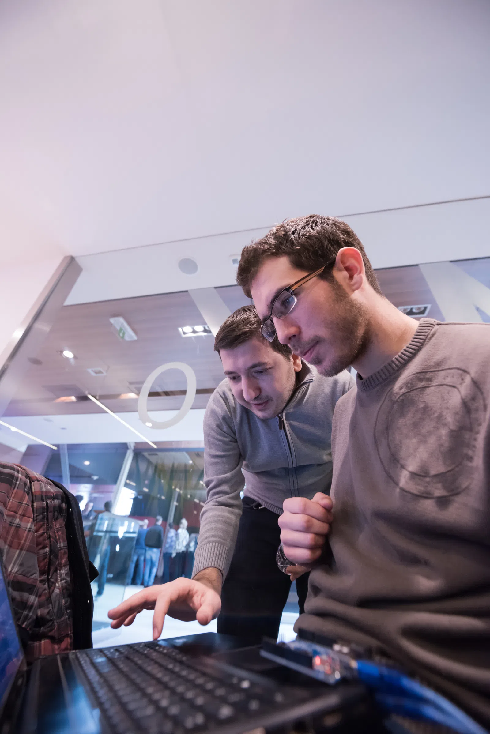 Two men collaborating on a laptop in a modern workspace, focused on their task.
