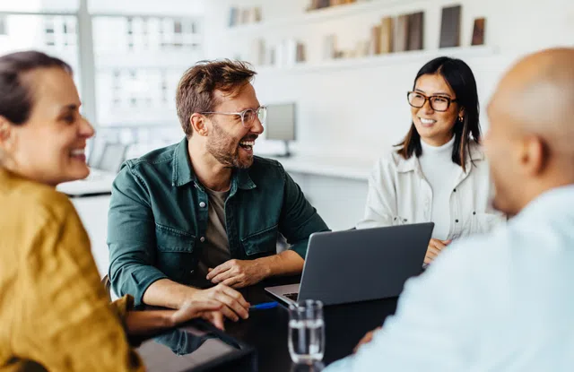 A diverse group of four people engaging in a lively discussion around a laptop in an office setting.