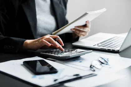 A business professional calculates finances with a calculator and reviews documents on a desk.