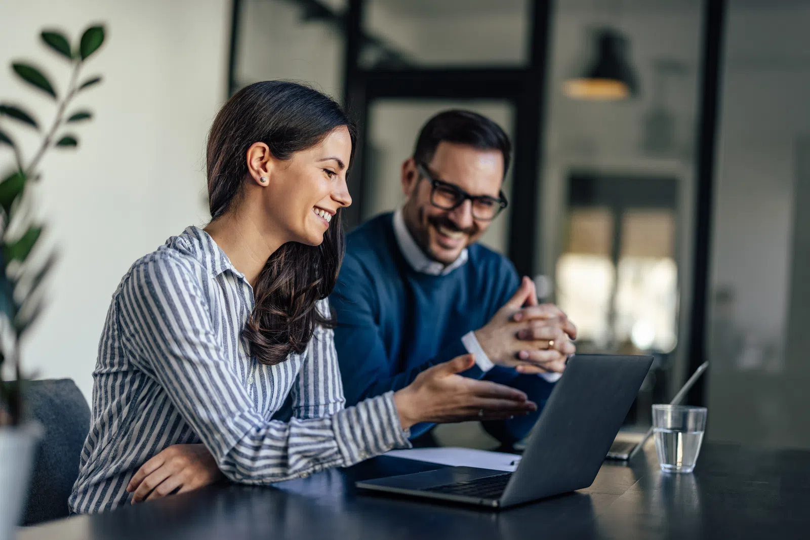 Two professionals collaborating at a desk with a laptop in a modern office setting.