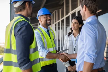 Construction professionals shaking hands, showcasing teamwork and collaboration on-site.