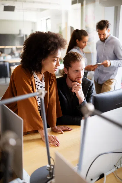 A diverse team collaborating in a modern office, focused on a computer screen and discussing ideas.