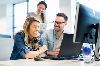 Group of cheerful colleagues collaborating in a modern office setting with computers.