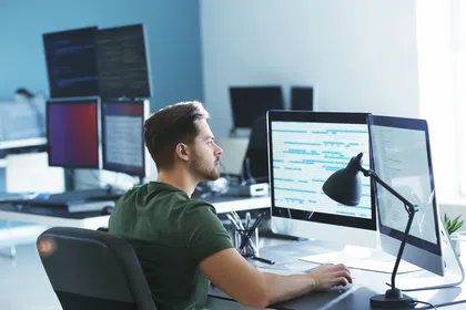 A focused man working at a desk with multiple computer monitors in a modern office setting.