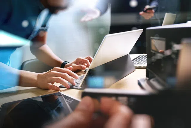 A person typing on a laptop surrounded by modern technology and office elements.