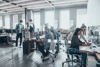 A modern office with coworkers collaborating at desks, showcasing teamwork in a bright space.