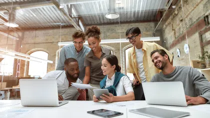 Group of diverse people collaborating in a modern office environment with laptops and tablets.