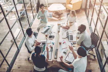 Team brainstorming in a modern meeting room with laptops and documents on a large table.