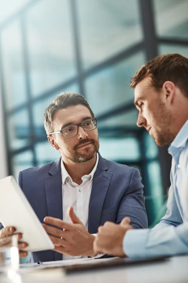 Two business professionals engaged in discussion with a tablet in a modern office setting.