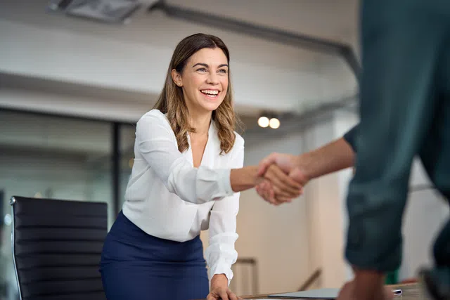 Businesswoman smiling and shaking hands in a modern office setting.