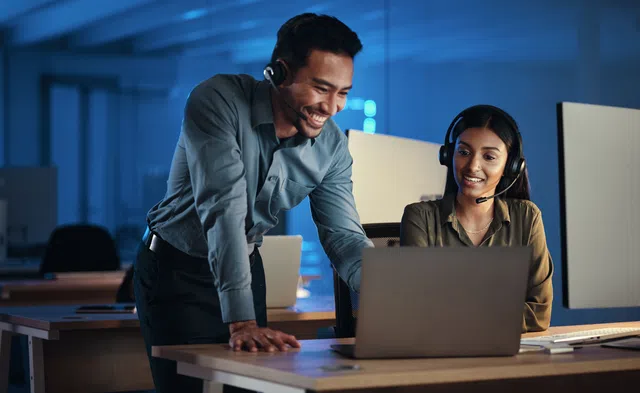 A man and woman in a modern office smile while collaborating over a laptop.
