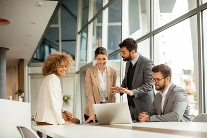 Four professionals collaborating around a laptop in a modern office setting.
