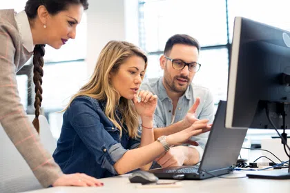 Three professionals collaborating on a project at a modern office, focused on a computer screen.