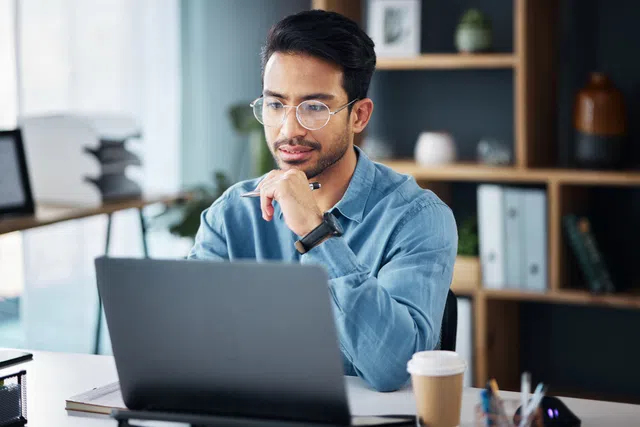 Concentrated man in glasses working on a laptop in a modern office setting.
