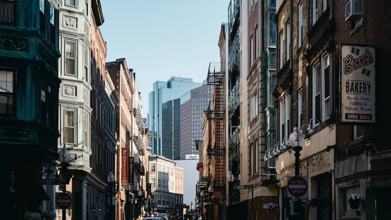 Historic city street lined with old brick buildings and modern skyscrapers in the background under a clear sky.