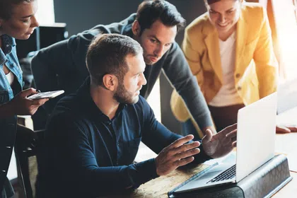 A group of professionals collaborating around a laptop in a modern office setting.