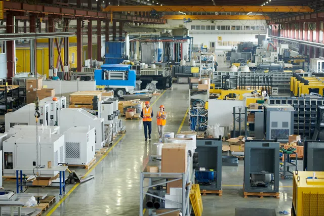 Workers in safety gear walking through a spacious manufacturing facility with machinery and equipment.