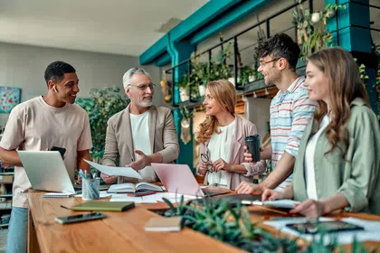 A diverse group of colleagues collaborating in a bright, plant-filled workspace.