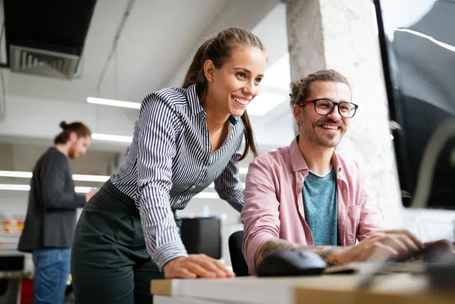 Two colleagues collaborate at a modern office workspace, smiling and engaging in discussion.