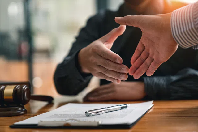 Two business professionals shaking hands over a contract on a wooden desk.