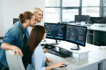 Three colleagues collaborating on computer coding in a modern office environment.