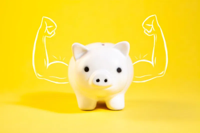 White piggy bank with drawn muscular arms on bright yellow background symbolizing strong savings.