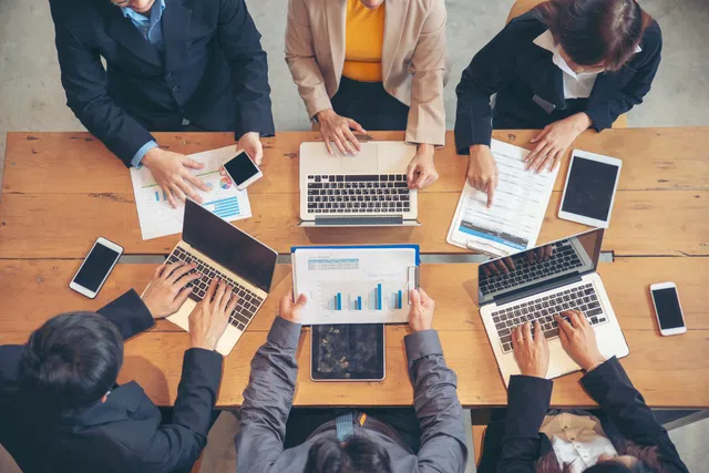 Aerial view of a business meeting with laptops, charts, and professionals collaborating on strategies.