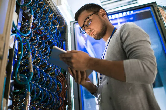 Technician working on server equipment, using a tablet to monitor systems in a data center.