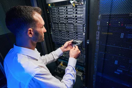 IT technician installing hardware in a data center server rack with blue lighting.