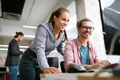 Two colleagues collaborating in a modern office, smiling and engaged with a computer.