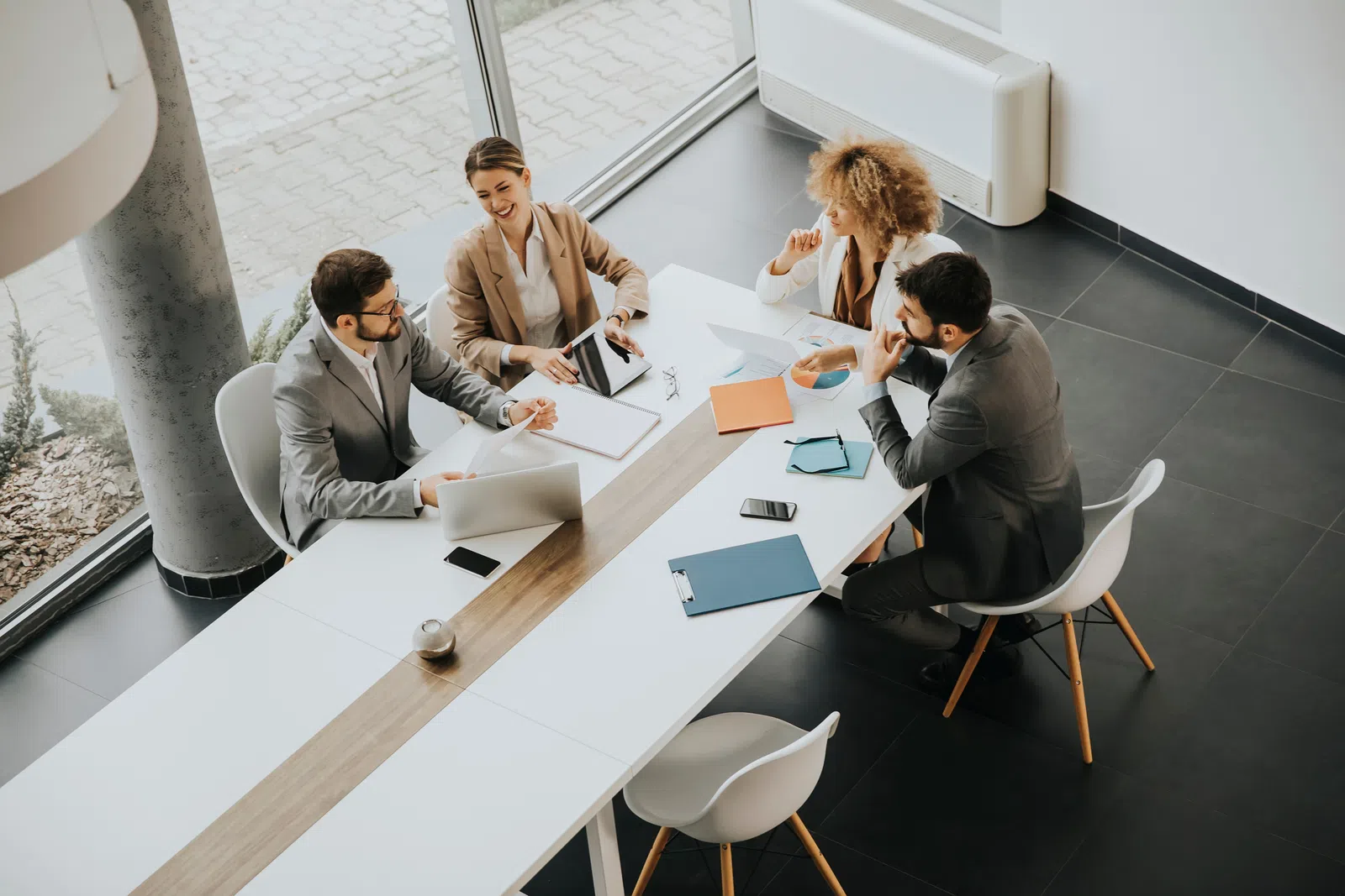 Four professionals in a modern office collaborating around a table with laptops and documents.