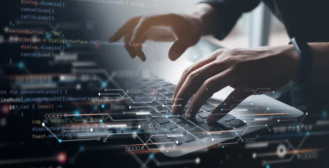 Close-up of hands typing on a laptop keyboard with code and digital graphics overlay.