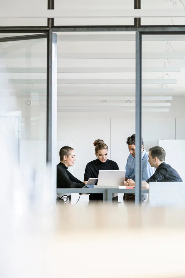 Four professionals collaborating around a laptop in a modern office environment.