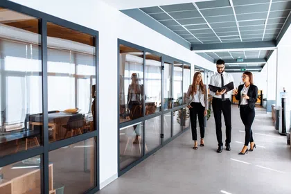 Professionals collaborating in a modern office corridor with large windows and contemporary design.