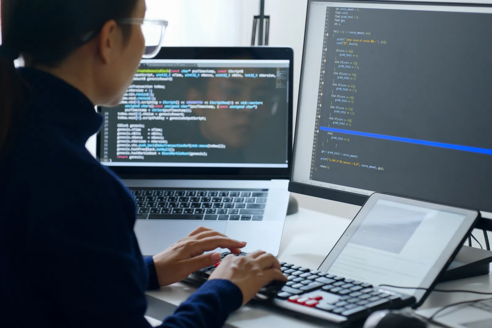 Person coding on multiple screens with laptop and tablet showing programming text and development environment.