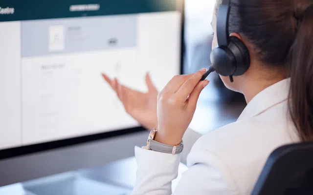 Woman in headset interacting with computer screen in a customer service setting.