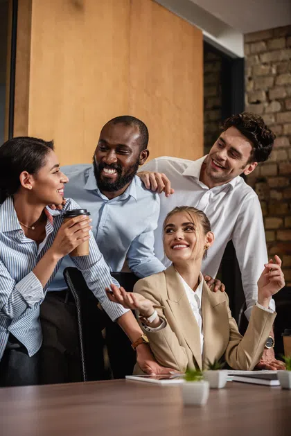 Four colleagues enjoying a light moment in a modern office setting, showcasing teamwork and camaraderie.