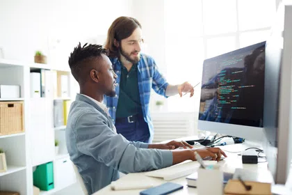 Two men collaborating on coding tasks at a computer in a modern office space.