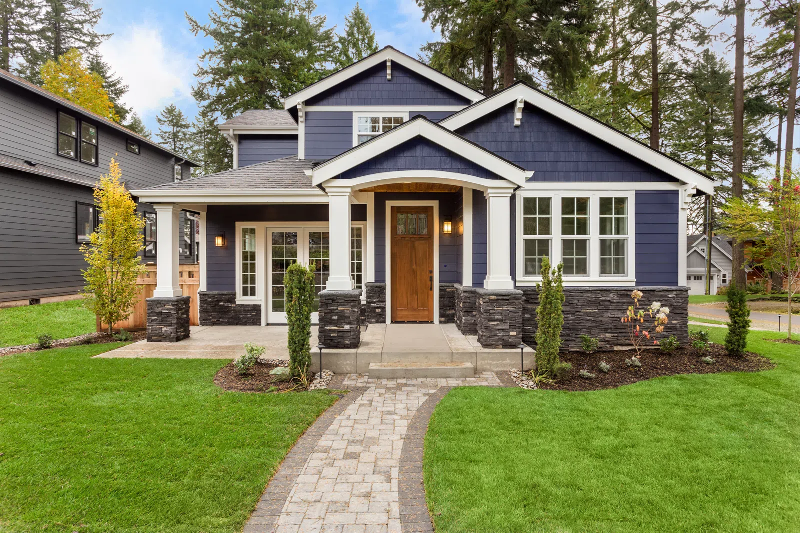 Stylish blue modern house with stone accents and lush green landscaping in a serene neighborhood.