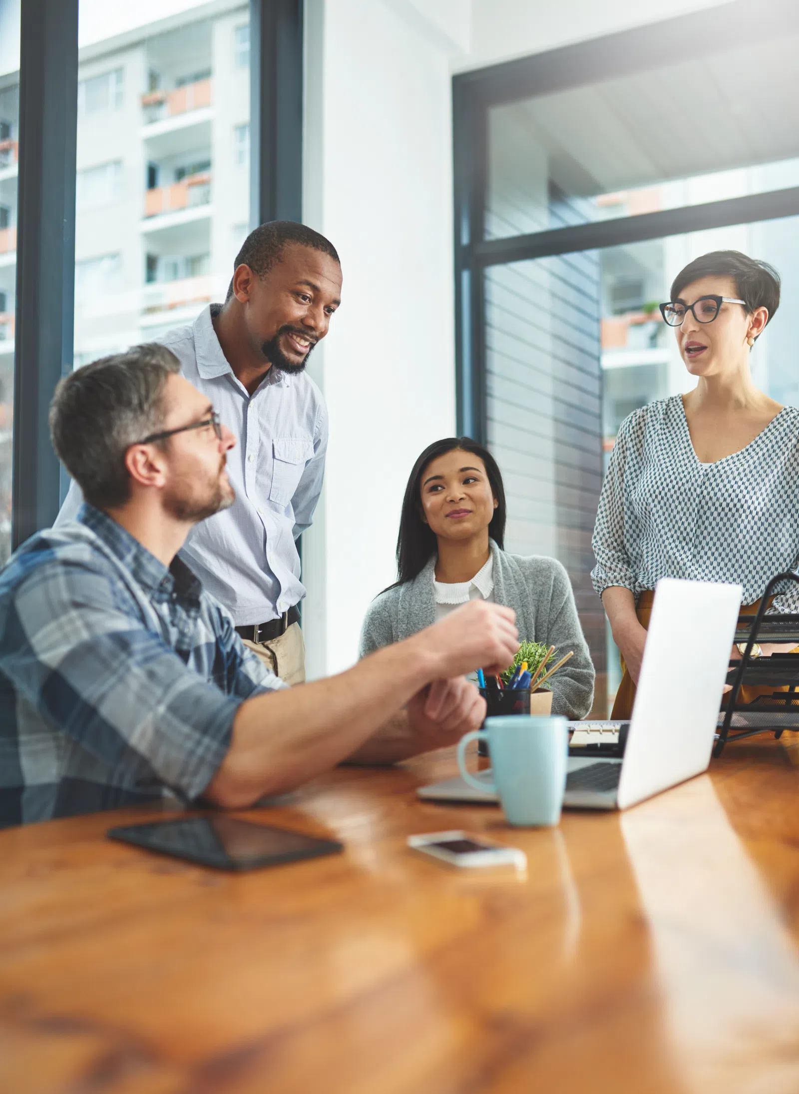 A diverse group of professionals collaborating in a modern office setting around a laptop.