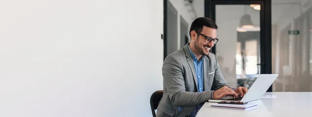 Smiling businessman working on a laptop in a modern office setting.