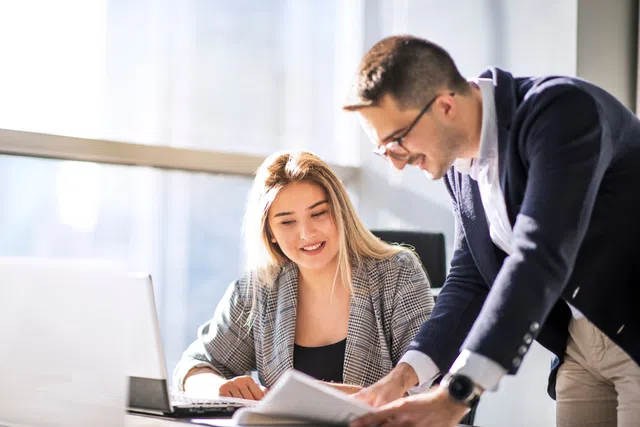 Professionals collaborating at a desk with a laptop and documents in a bright office environment.