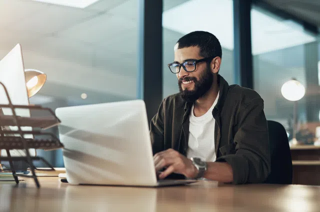 Smiling man working on a laptop in a modern office environment.