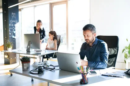 Three professionals working in a bright office space with computers and fresh plants.